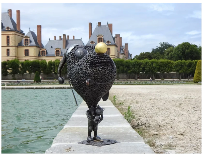 Une sculpture de l'agence artistique exposée au bord d'un bassin, devant un château